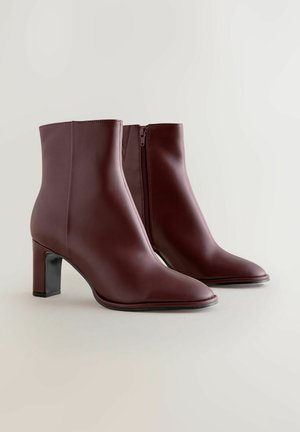 Bordeaux enkellaarsjes met een soepel lederen textuur, spitse neus en een blokhak. Voorzien van een zijrits en een slanke, moderne silhouet.