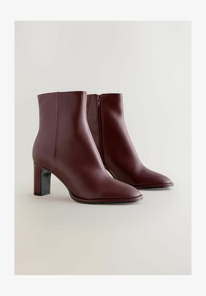 Burgundy ankelstövlar med en slät lädertextur, spetsig tå och klack med blockform. Har en sidoglider och en elegant, modern silhuett.