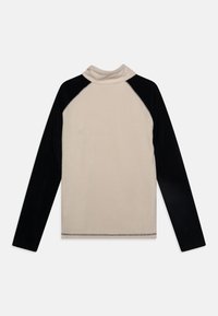 Bluzka z długim rękawem, o beżowym korpusie i czarnych rękawach raglanowych. Posiada stójkę i widoczne szwy wzdłuż dołu. Miękka tekstura materiału.