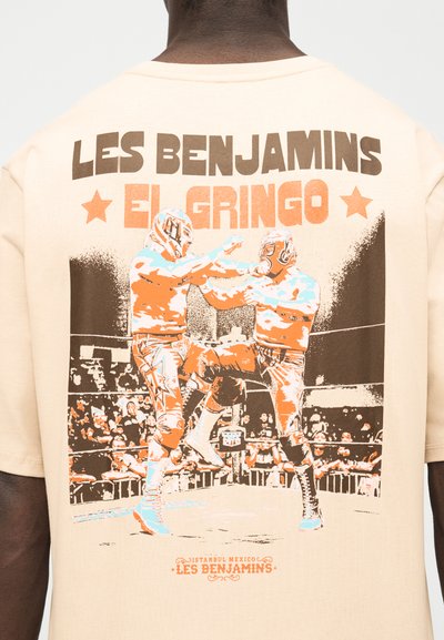 Δύο μάσκες παλαιστές σε ρινγκ, στη μέση της δράσης, με το κείμενο "LES BENJAMINS EL GRINGO" πάνω και πλήθος στο παρασκήνιο.