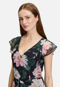 Robe fleurie avec un fond sombre, présentant un décolleté en V, des manches courtes et de grandes fleurs roses avec des feuilles vertes, fabriquée en tissu léger.