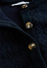 Ciemnoniebieski sweter z dzianiny, charakteryzujący się teksturowaną powierzchnią, dużymi okrągłymi złotymi guzikami oraz złożonym kołnierzem.