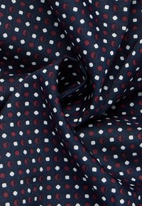 Tessuto blu navy con superficie testurizzata caratterizzata da un motivo di piccoli punti e esagoni rossi, bianchi e beige distribuiti uniformemente.