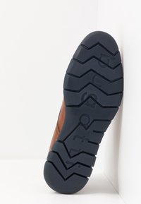 Chaussure en cuir marron avec une tige texturée et une semelle en caoutchouc foncé présentant une bande de roulement en zigzag et un nom de marque embossé. Taille 42 indiquée.