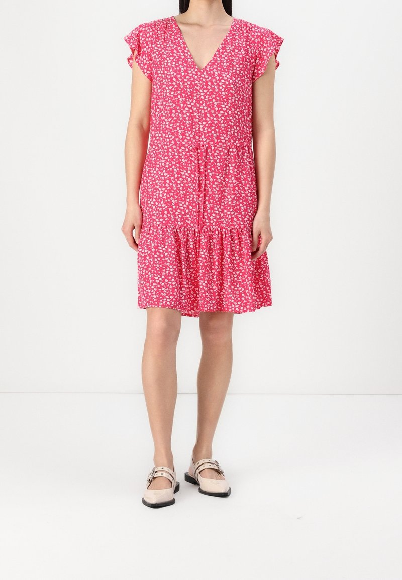 Rosa geblümtes Kleid mit kurzen, gerafften Ärmeln, V-Ausschnitt und Stufenrock. Der Stoff hat eine leichte, strukturierte Optik. Kombiniert mit flachen Schuhen.