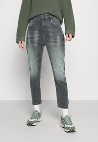 Grå denimjeans med en lätt sliten finish, rak skärning och femfickorsdesign, kombinerat med en grön tröja och sneakers.