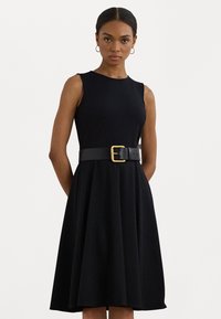 Melnas bez piedurknēm kleita, izgatavota no gludas auduma, ar izvērstu svārku un pieguļošu jostasvietu, kas akcentēta ar platu melnu jostu un zelta sprādzi.