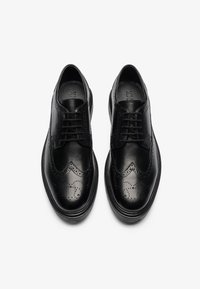 Schwarze Leder-Wingtip-Schuhe mit glatter Oberfläche, dekorativen Brogue-Lochungen und einem runden Zehendesign. Mit Schnürverschluss.