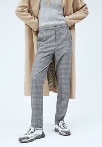 Szare spodnie w kratę o dopasowanym kroju, z paskami na pasek, zamkiem błyskawicznym oraz gładkim przodem, zestawione z białymi trampkami i beżowym płaszczem.