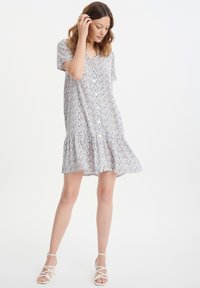 Vestido floral de manga corta en blanco, con cierre de botones en la parte delantera, dobladillo con volantes y un colorido estampado floral con acentos en azul y naranja.