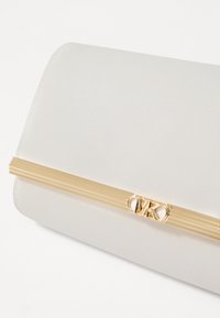 Pochette blanche texturée avec un accent linéaire en ton doré et un logo gravé. Tissu lisse avec des bords arrondis.