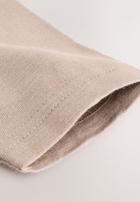 Tissu beige à la texture douce, avec un ourlet net et de légers détails de couture. Le matériau semble léger et respirant.