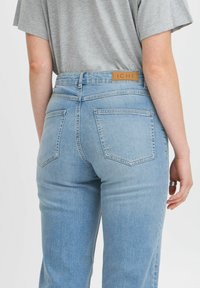 Helle blaue Jeans mit hoher Taille, Fünf-Taschen-Design und Lederlabel auf der Rückseite. Der Stoff wirkt weich und hat eine glatte Textur.