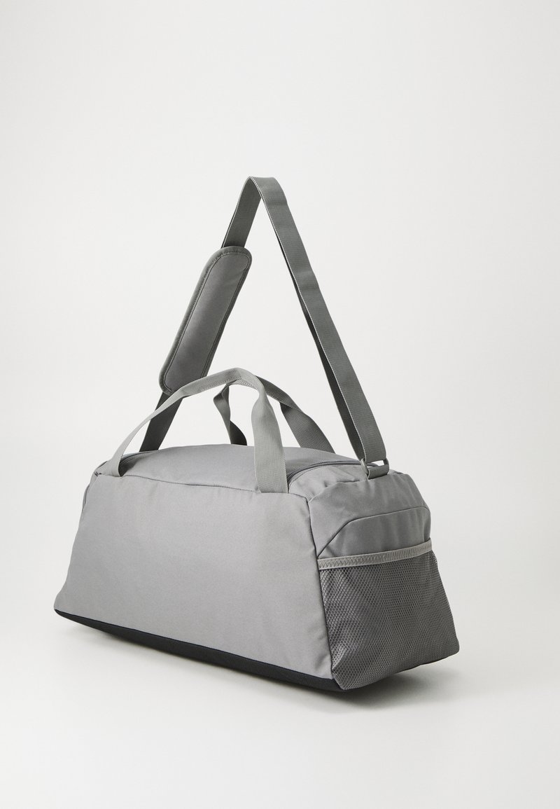 Sac de sport gris avec poignées de transport doubles, bandoulière rembourrée, poche latérale en mesh texturé et surface extérieure lisse.