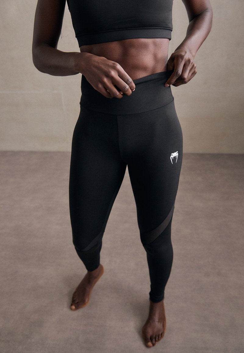 Leggings neri a vita alta con pannelli in rete, dotati di un logo sul lato. Realizzati con materiale elastico, progettati per comfort e flessibilità.