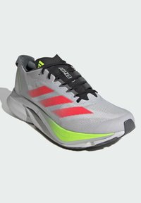 Grauer Sportschuh mit einer strukturierten Oberseite, schwarzen Schnürsenkeln, roten Streifen und grünen Akzenten. Verfügt über ein schlankes Design und eine gepolsterte Sohle.