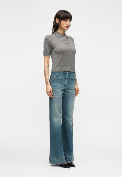 Polo gris à manches courtes avec col et détails de boutons, associé à un jean bleu clair taille haute à jambes larges et des talons noirs pointus.