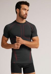 Fitted černé sportovní tričko s krátkým rukávem a červenými švy, s texturovanou tkaninou a kulatým výstřihem.