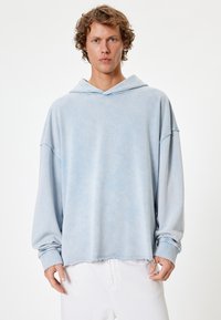 Sudadera de gran tamaño en azul claro con una textura desvanecida, hombros caídos y un dobladillo deshilachado. Tejido suave con un diseño relajado.