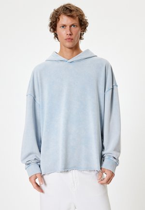 Sudadera de gran tamaño en azul claro con una textura desvanecida, hombros caídos y un dobladillo deshilachado. Tejido suave con un diseño relajado.