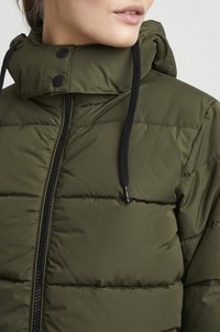Olivgrön puffjacka med hög krage, dragkedja fram och svarta dragsnören. Har quiltat mönster och tryckknappar.