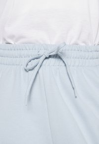 Jogging léger bleu avec taille élastique et cordon de serrage, fabriqué en tissu doux, présentant une texture lisse et des plis subtils.