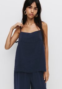 Top senza maniche di colore blu navy, con spalline sottili e scollatura quadrata, caratterizzato da una vestibilità ampia e una texture morbida, con dettagli minimali.