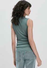 Top sans manches ajusté en tissu vert doux avec une texture lisse. Associé à un jean bleu clair à coupe décontractée avec poches arrière.