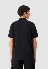 Svart polo-skjorte, korte ermer, myk tekstur, standard krage, ingen synlige logoer eller mønstre, kombinert med svarte cargo-bukser.