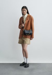 Hnědá kordurová sako na krémovém pleteném svetru, doplněné khaki šortkami. Černá kabelka přes rameno s řetízkem, černé loafers a bílé ponožky.