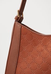 Bolso de cuero marrón con patrones circulares de flores en relieve y herrajes dorados que conectan la correa de hombro ajustable.