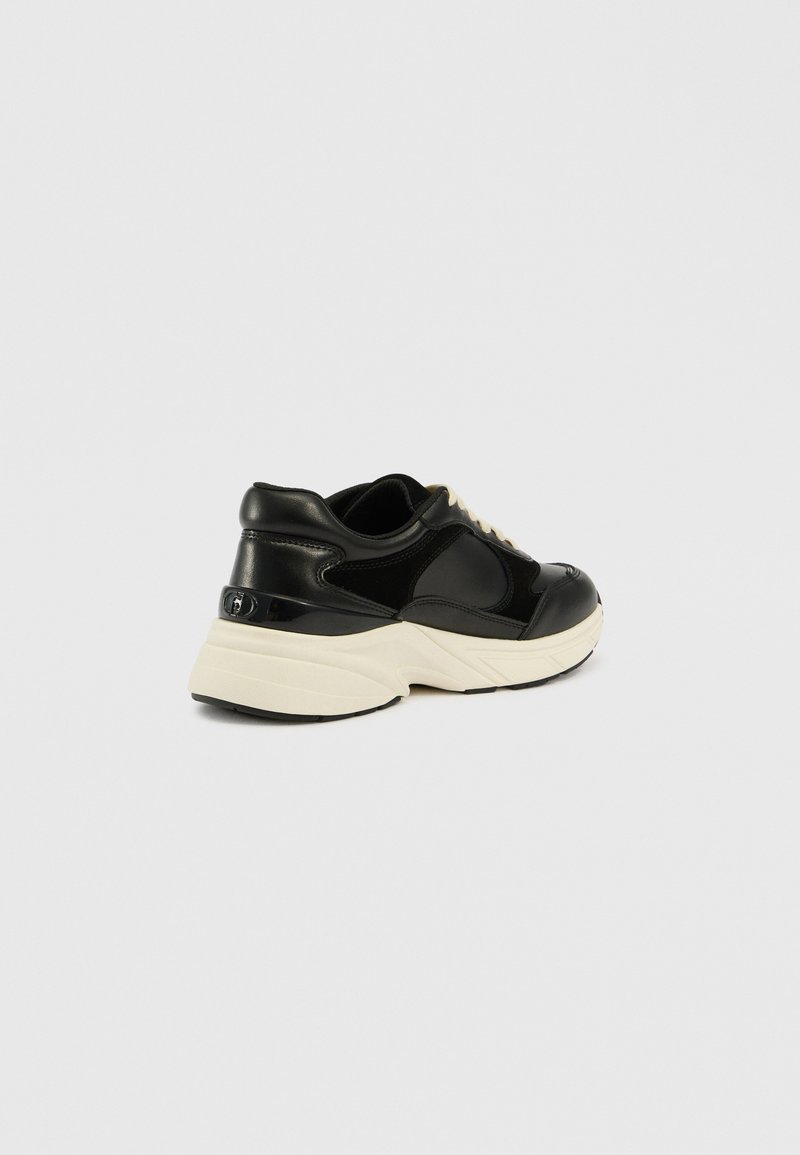 Schwarzer Sneaker mit einem glatten Leder-Obermaterial, cremefarbener Sohle, runder Form und kontrastierenden Texturen sowie einem dezenten Logo-Detail.