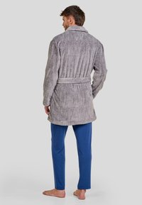Bata gris con patrón de espiga y cinturón; textura suave. Combinada con pantalones azules. La bata tiene un cuello de chal y mangas largas.