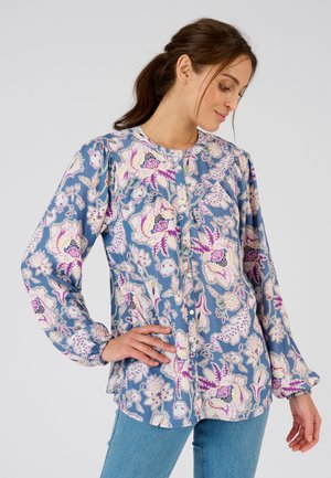 Camisa de manga larga con un patrón floral en azul, con acentos en púrpura y blanco, que presenta un escote redondo y cierre de botones en la parte delantera. Textura de tela suave.