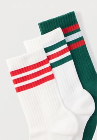 Τρεις κάλτσες σε λευκό, κόκκινο και πράσινο χρώμα. Η κάθε μία έχει ριμπ υφή με δύο οριζόντιες ρίγες σε διαφορετικά σχέδια.