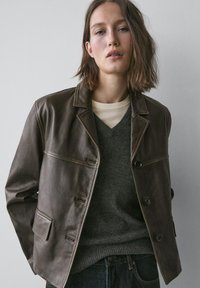 Brun læderjakke med klassisk krave og knaplukning. Har en glat tekstur, sidelommer og en skræddersyet silhuet.