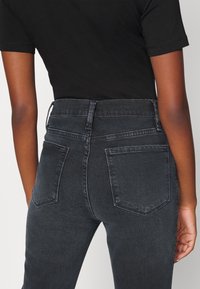 Jeans in denim nero a vita alta, con una texture liscia, tasche posteriori e un design di cucitura pulito.