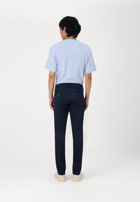 Camisa de manga corta azul claro con cuello redondo, combinada con pantalones de corte slim de color azul marino y zapatillas de colores claros, vista desde la parte de atrás.