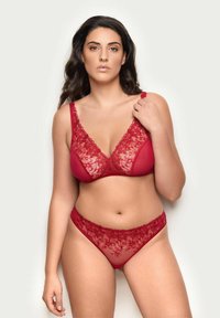 Czerwony zestaw bielizny składający się z biustonosza bralette i dopasowanego stringów. Biustonosz ma wstawki z kwiatowej koronki oraz regulowane ramiączka; materiał jest gładki z przezroczystymi panelami.