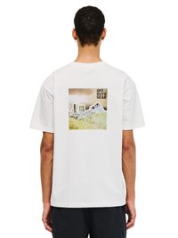 Mann trägt ein weißes T-Shirt mit einer Grafik von Gebäuden, Bergen und dem Text "OFF DUTY GEAR" auf dem Rücken, steht vor einem weißen Hintergrund.