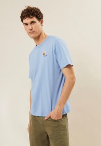 Camiseta de algodón azul claro con cuello redondo, mangas cortas y un pequeño diseño de arcoíris bordado en el pecho.