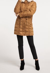 A brown puffer coat with a detachable faux fur hood, zippered front, cinched waist, and textured quilted pattern. Black fitted pants and ankle boots.