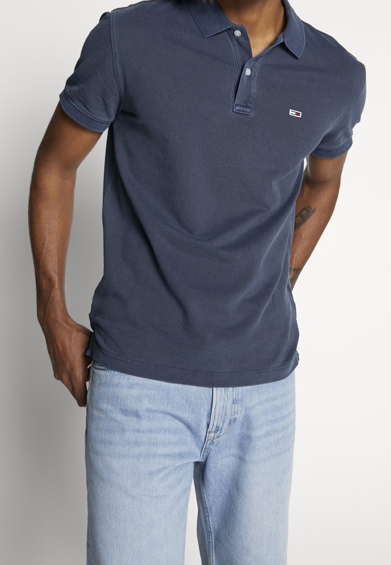 Polo blu navy in cotone, con chiusura a due bottoni, maniche corte e un piccolo logo sul petto. Vestibilità classica.