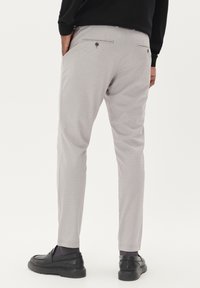 Világosszürke, finoman texturált, szabott nadrág hátsó zsebekkel, karcsú fit-tel és gombos díszítéssel. Fekete cipővel párosítva.