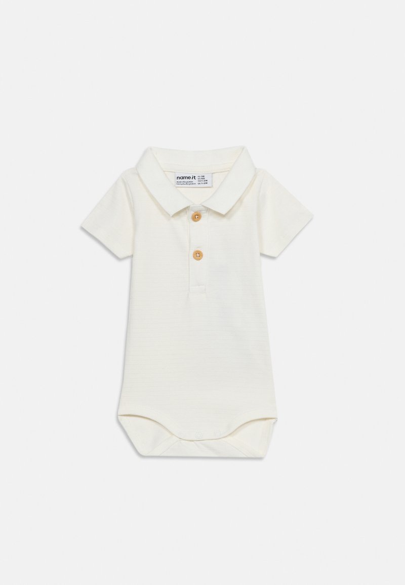 Combinaison pour bébé manches courtes couleur crème, avec col et deux boutons en bois sur la patte de boutonnage, posée à plat sur fond blanc.