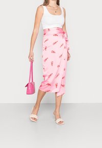 Jupe portefeuille en satin rose avec un motif de homard, nouée à la taille avec une ceinture assortie. Associée à un débardeur blanc et un sac à main rose.