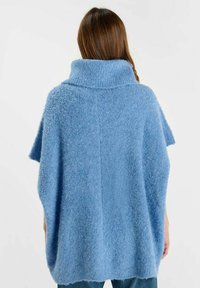 Poncho di lana azzurro chiaro con collo alto, texture morbida, maniche corte e design sventagliato ai lati, che evidenzia un aspetto accogliente.