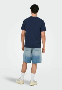 Mørkeblå kortærmet t-shirt, afslappet pasform, parret med lyse denimshorts med et falmet mønster. Hvide sokker og grå sportsko fuldender looket.