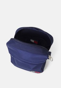 Mochila de tela azul marino con cierre en la parte superior, bolsillo exterior y una textura suave. El interior presenta una etiqueta de logo en rojo, blanco y azul.