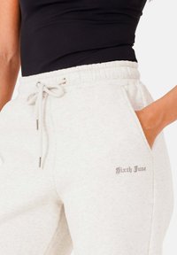 Hellgraue Sweatpants mit elastischem Bund und Kordelzug sowie seitlichen Taschen, akzentuiert durch ein dezentes gesticktes Logo am Bein.